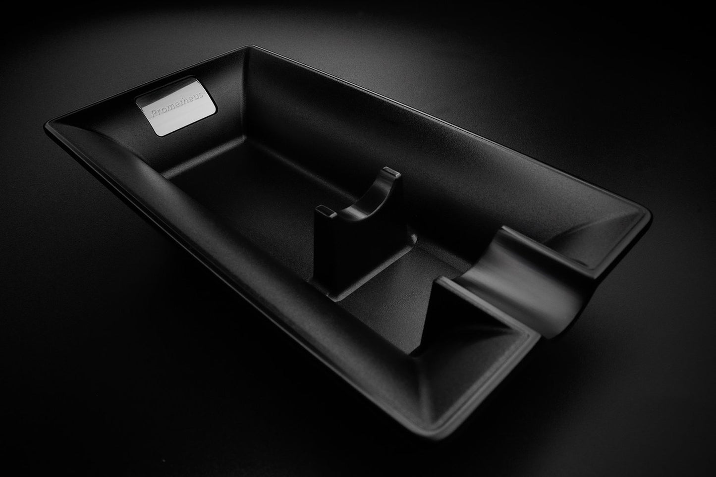 A modern black matte metal ashtray.  The ashtray is sleek with a single cigar ledge. The brand is Prometheus.