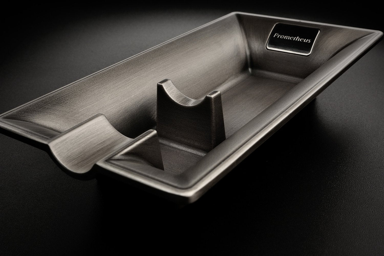 A modern brushed chrome metal ashtray.  The ashtray is sleek with a single cigar ledge. The brand is Prometheus.