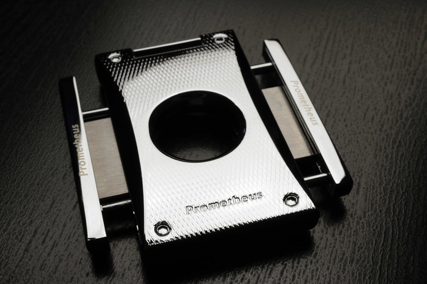 A black chrome metal cigar cutter from the Prometheus brand of accessories. The sides of the cutter come out and are squeezed to create the sleek and precise cut. The design is etched, elegant, modern and good-looking. 